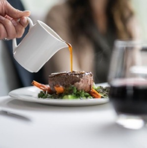 Host pouring sauce onto steak during lunch service