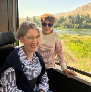 A woman sitting in a wheelchair beside her mother with greenery outside the window while onboard the Rocky Mountaineer train.